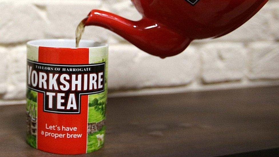 Red teapot pouring tea into a Yorkshire Tea mug on a wooden surface.