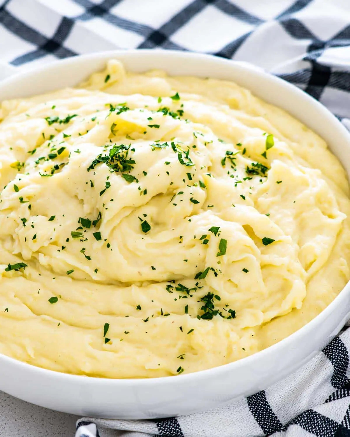 Mashed potatoes with green herbs in a white bowl on a checkered cloth