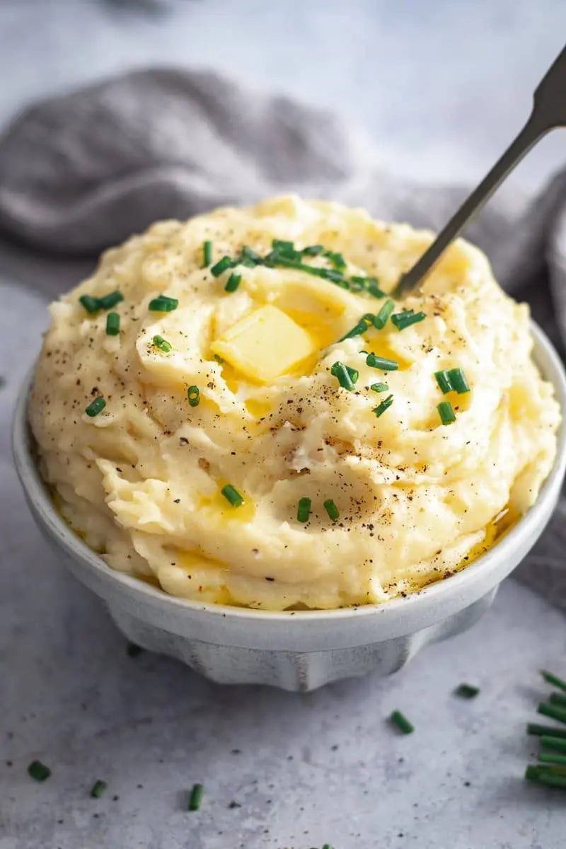 Mashed potatoes with butter and chives in a white bowl on a gray surface.
