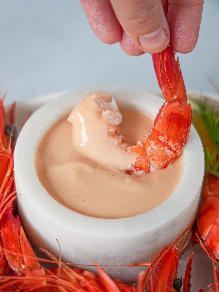 Shrimp being dipped into a bowl of mayonnaise with a hand holding it above.
