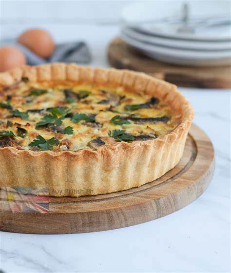 Quiche on a wooden board with eggs and plates in the background
