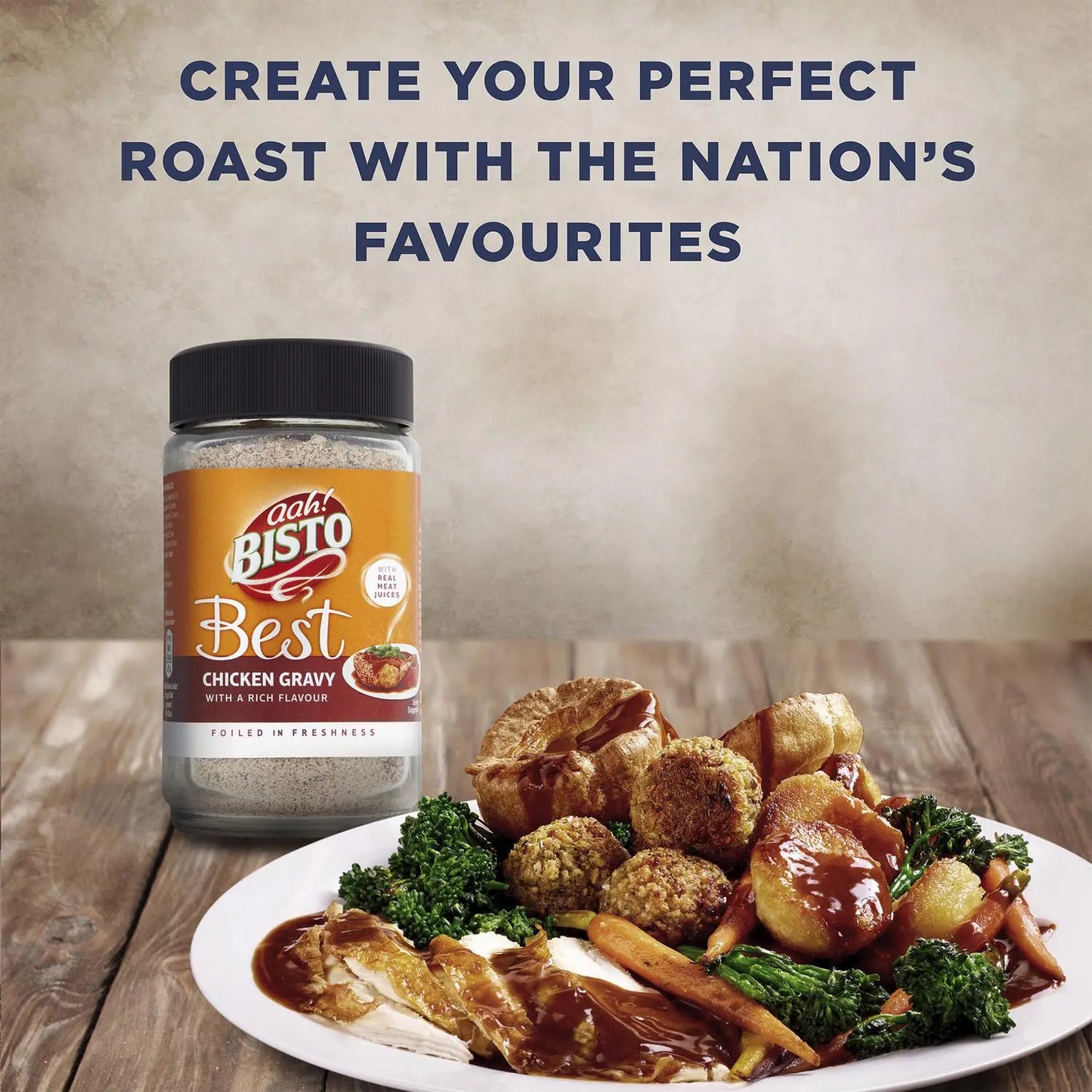 Bisto Best Chicken Gravy jar with a roasted chicken and vegetable dish on a wooden table.