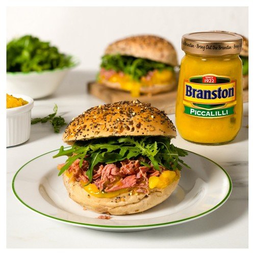 Burger with Branston Piccalilli on a white plate with a jar of Branson Piccalilli in the background.