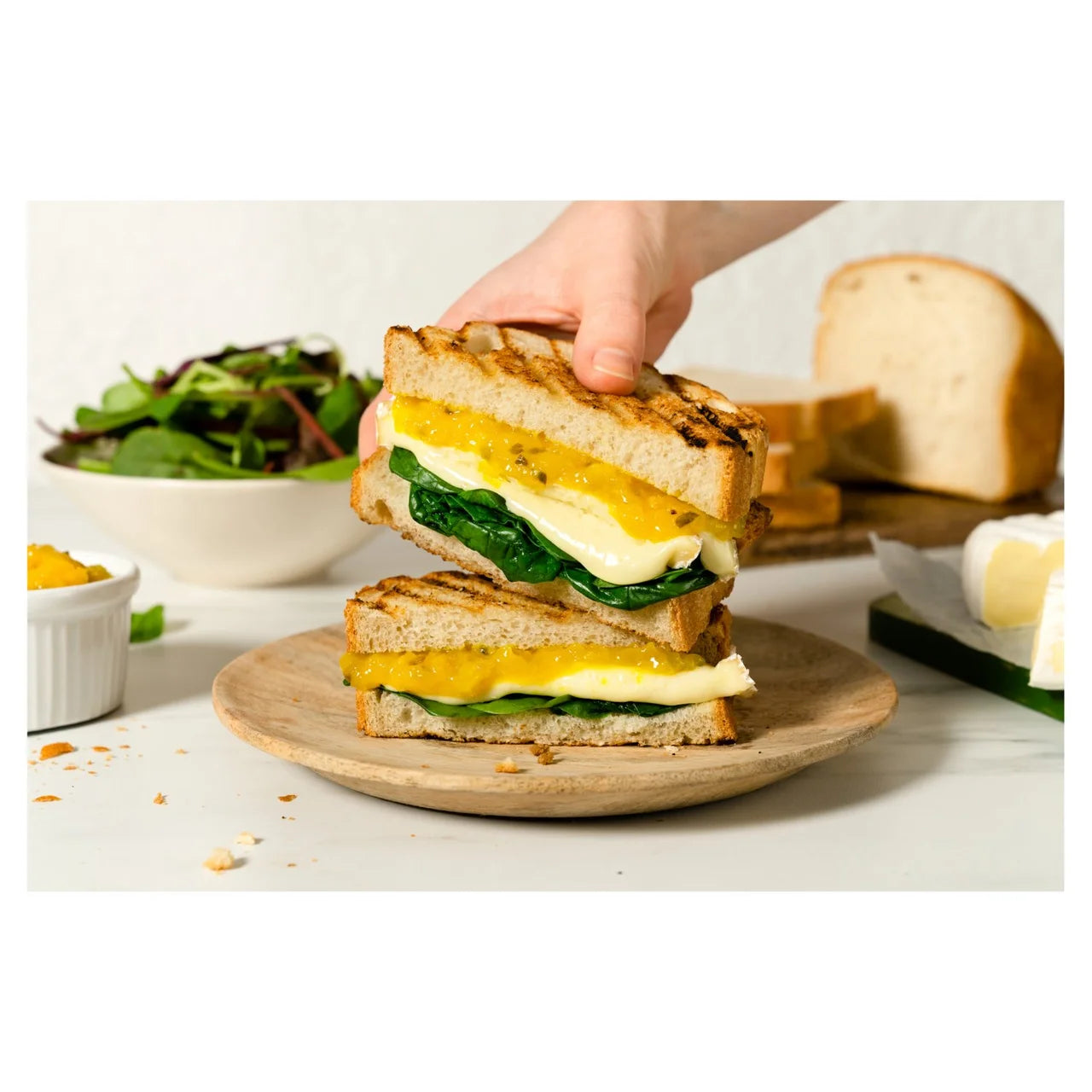 Stack of grilled sandwiches with egg and spinach on a wooden plate, with a hand reaching for one.