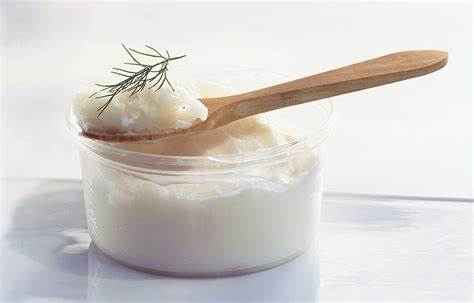 Jar of white cream with a wooden spoon and rosemary on a white background