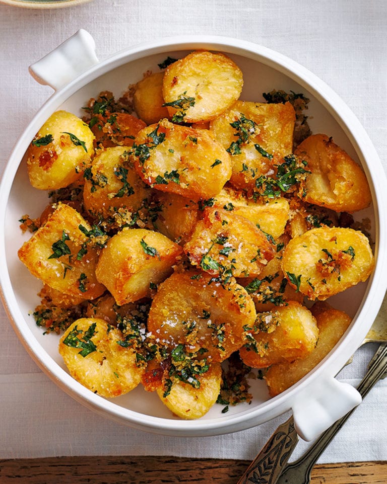 White bowl filled with roasted potatoes garnished with herbs on a light background