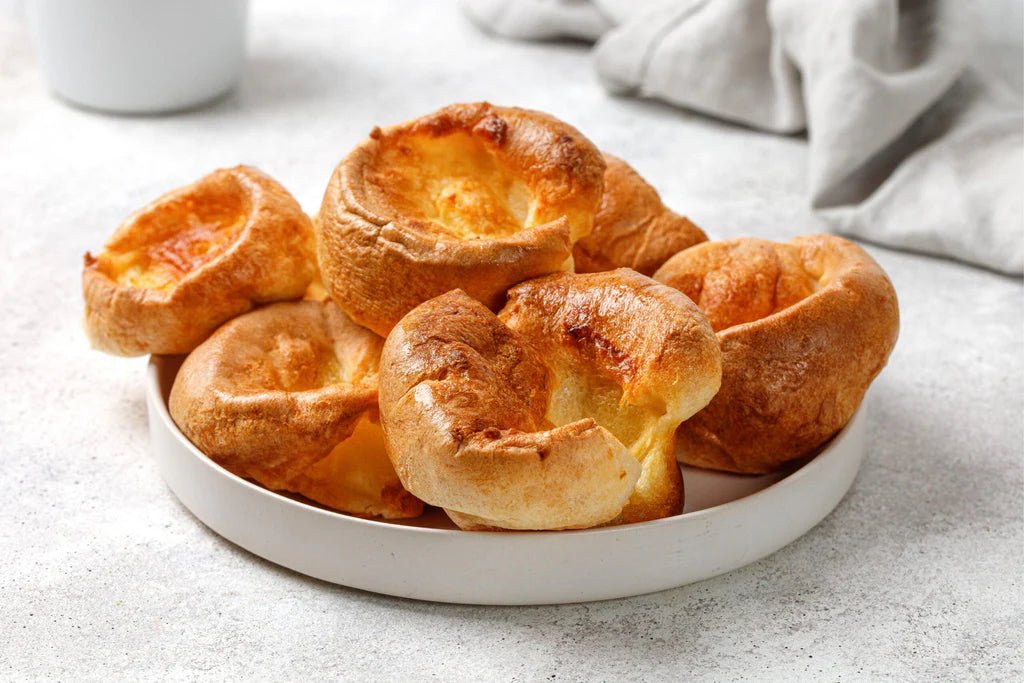 Plate of Yorkshire puddings on a light surface with a white cup and gray towel in the background.