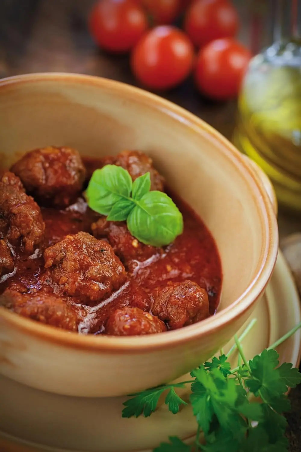 Bowl of meatballs in a red sauce with fresh basil leaves, set against a rustic background.