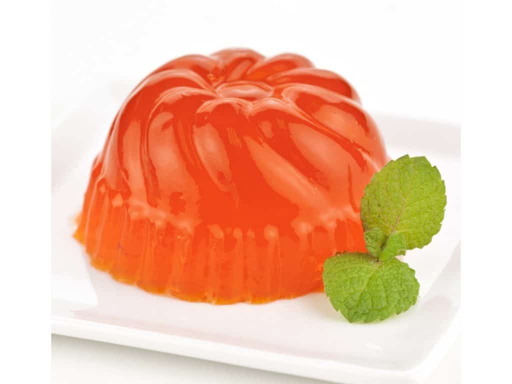 Orange jelly mold on a white plate with a sprig of mint
