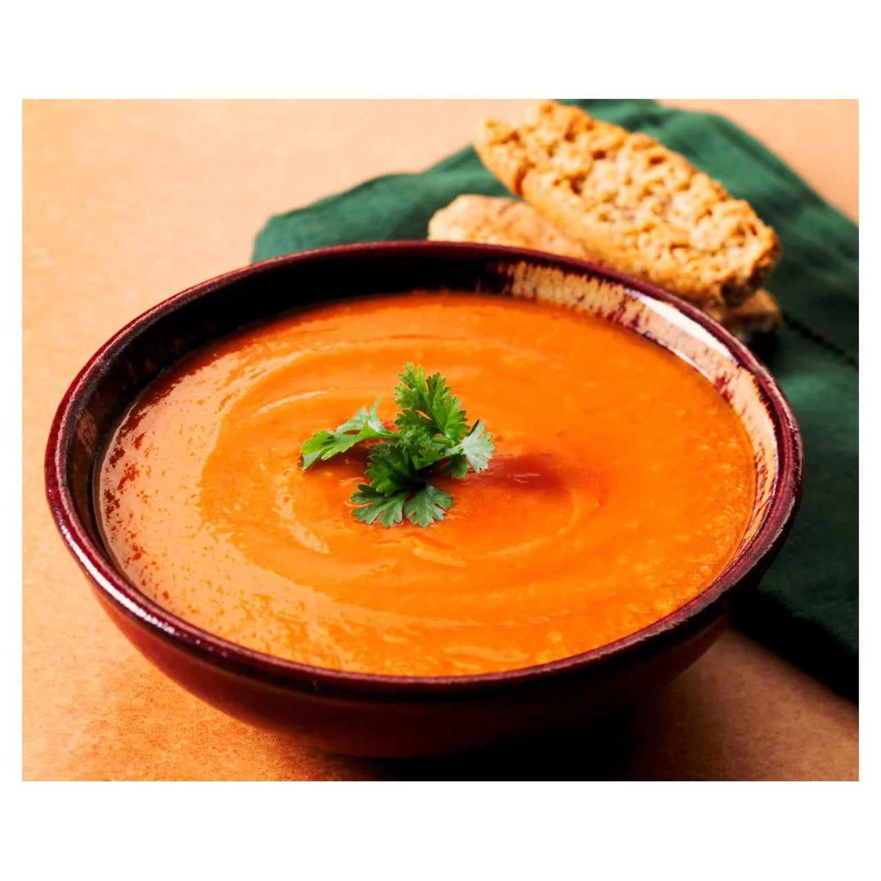 Bowl of tomato soup with a sprig of parsley on a wooden table.