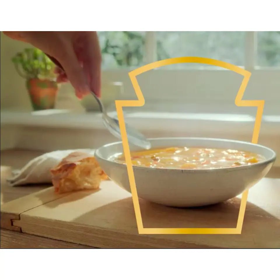 Bowl of soup with a hand holding a spoon, placed on a wooden surface with a blurred background.