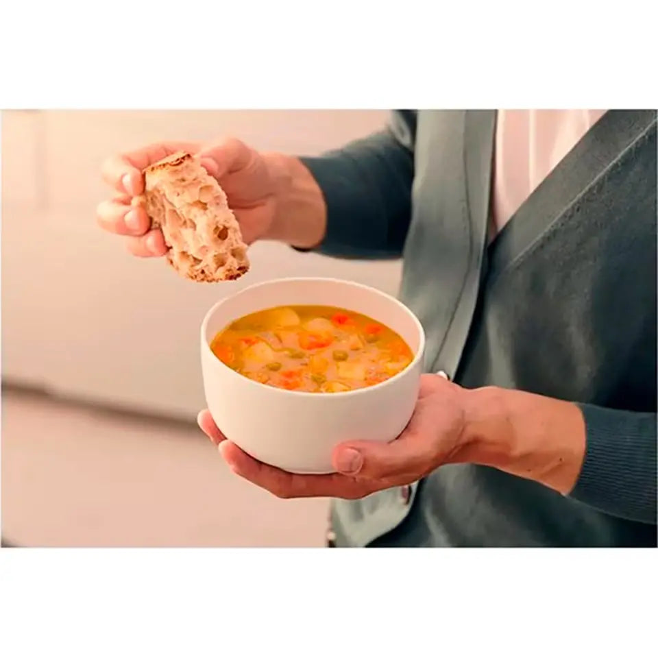 Person holding a bowl of soup and a piece of bread.