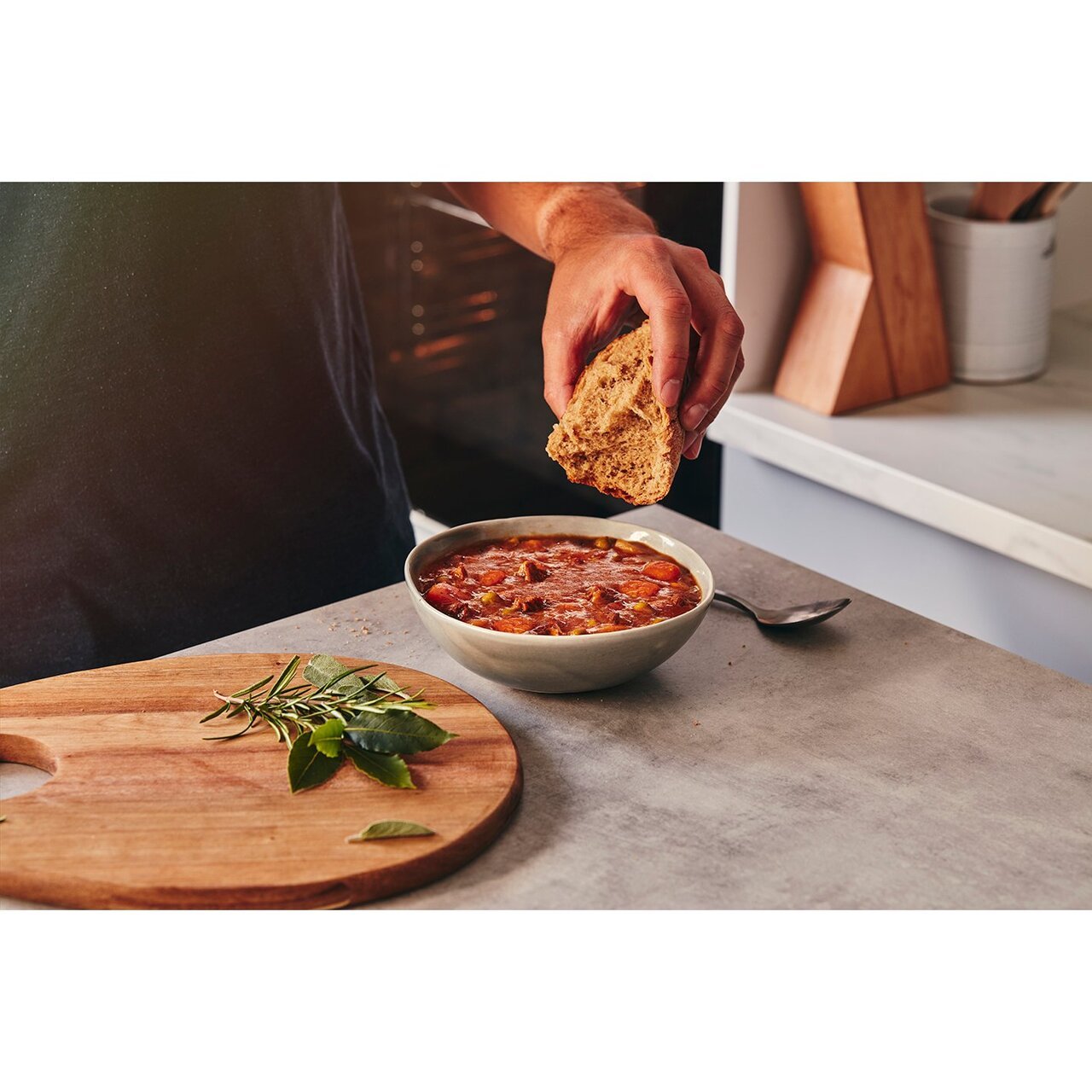 Person dipping bread into a bowl of chili on a kitchen counter.