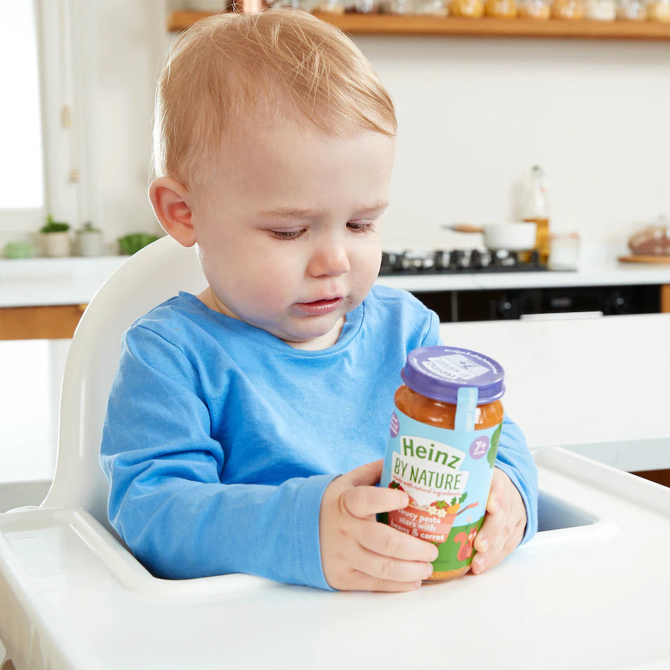 Child in a high chair holding a Heinz baby food jar in a kitchen setting