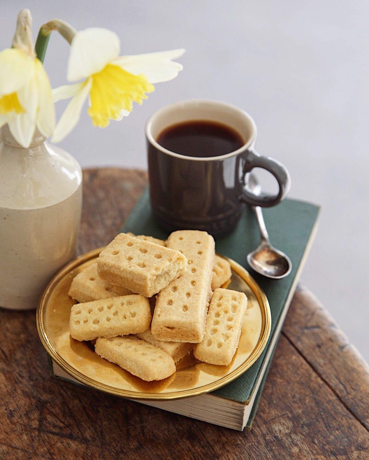 Plate of shortbread cookies with a cup of coffee and a vase of flowers on a wooden table.