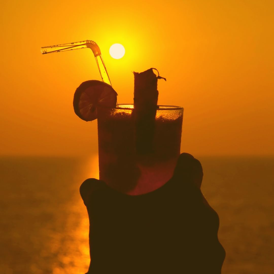 Hand holding a cocktail with sunset in the background