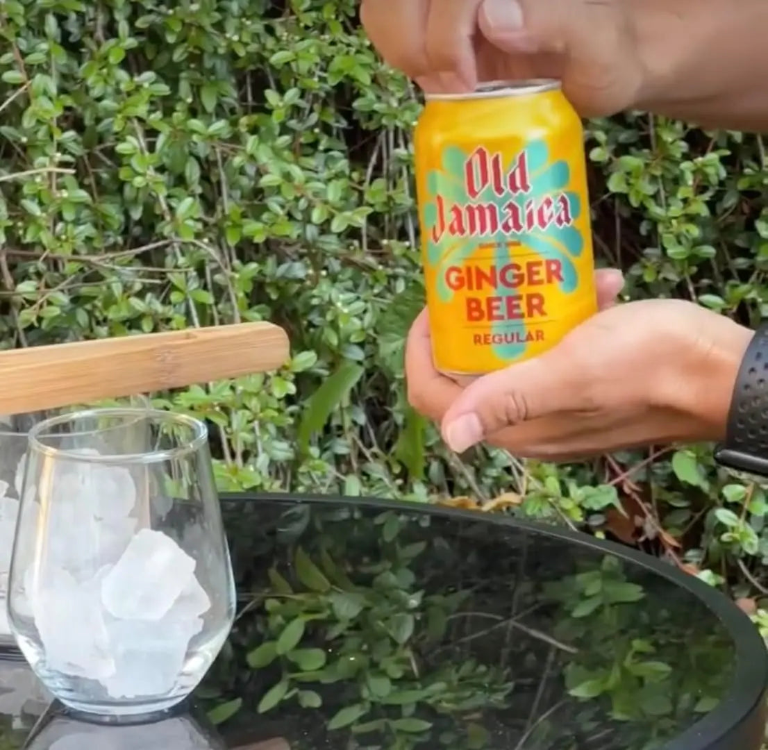 Hand holding a can of Old Jamaica Ginger Beer with a glass of ice in the background.