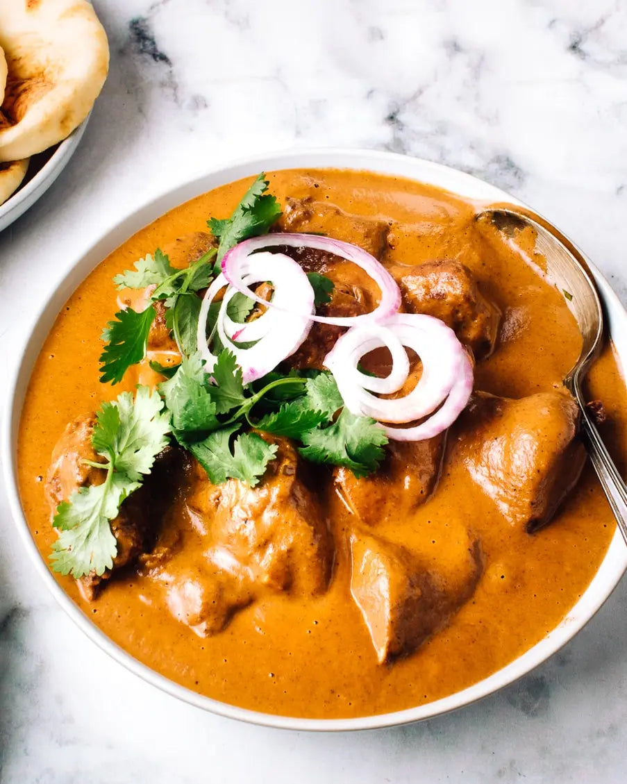 Bowl of creamy curry with chicken, garnished with onions and cilantro, on a marble surface.