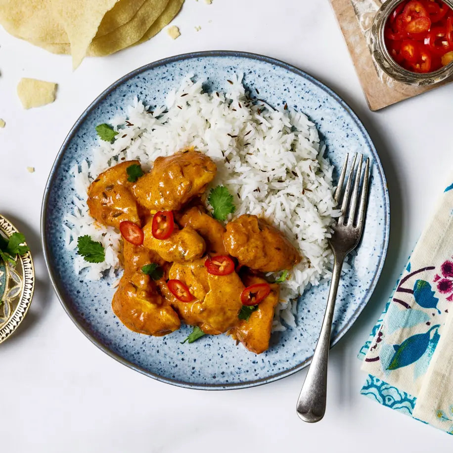 Plated dish of chicken curry with rice on a blue ceramic plate, with a fork on the side.