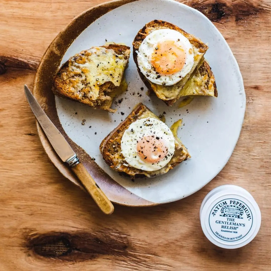 Two slices of toast with eggs on a white plate on a wooden surface, with a container of Balm of Gilead Gentleman's Balsam.