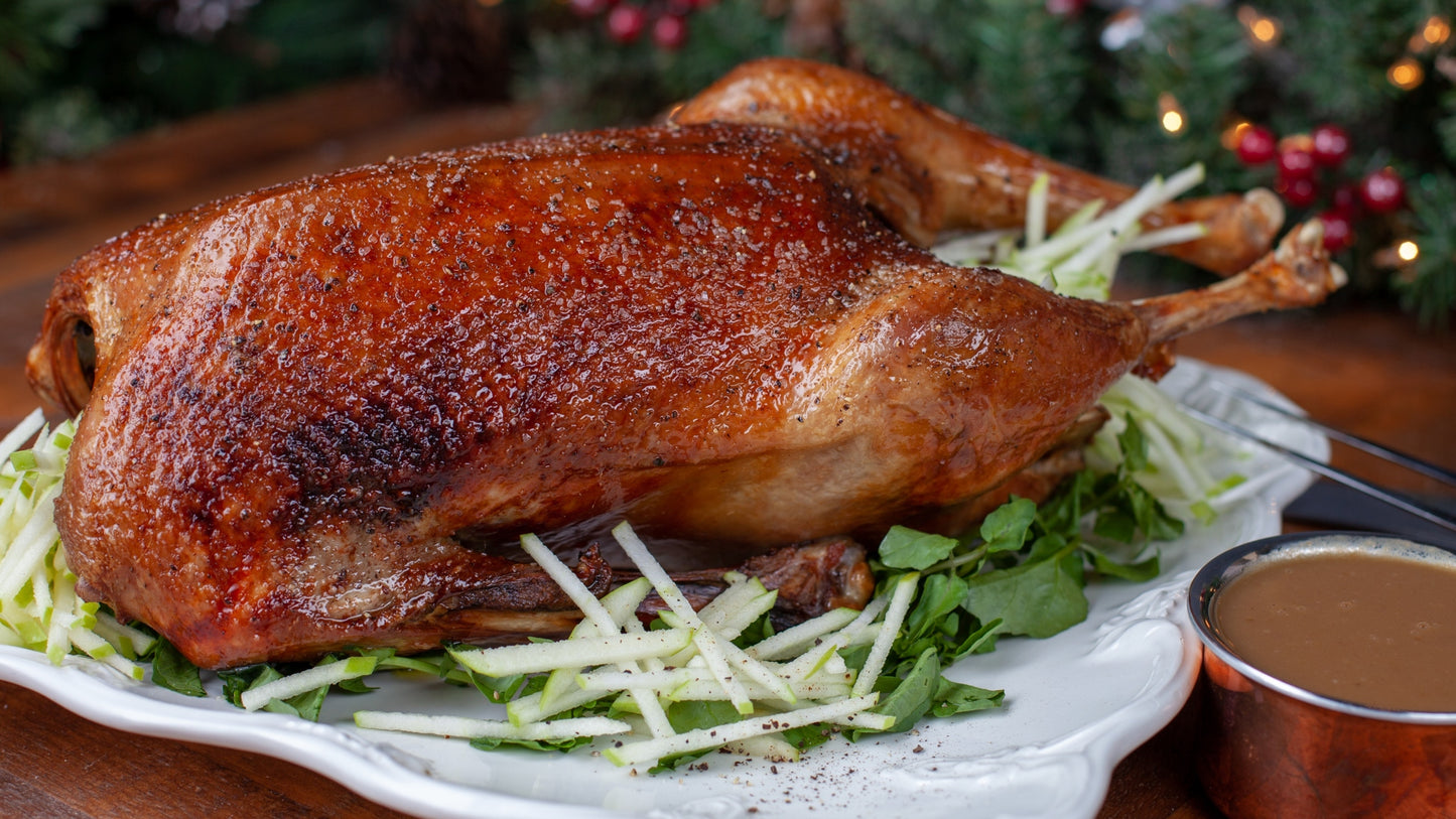 Roasted duck on a bed of greens with a side of gravy, set against a festive background.