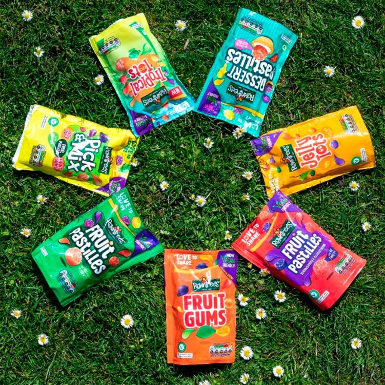 Assorted packets of fruit snacks on a grassy background with flowers.