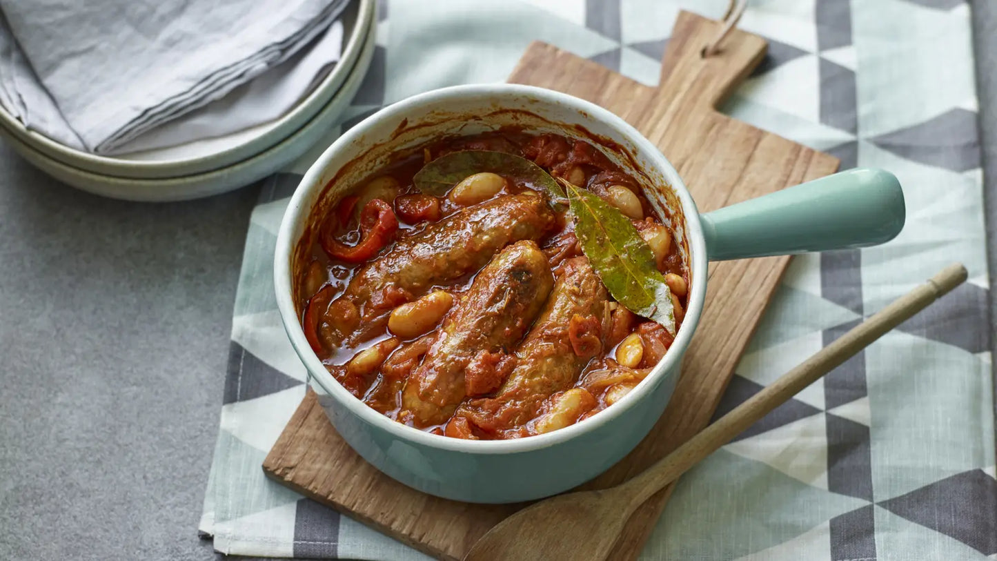 Casserole dish with sausages and beans on a wooden board