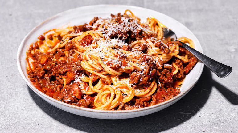 Spaghetti dish with meat sauce on a white plate against a gray background