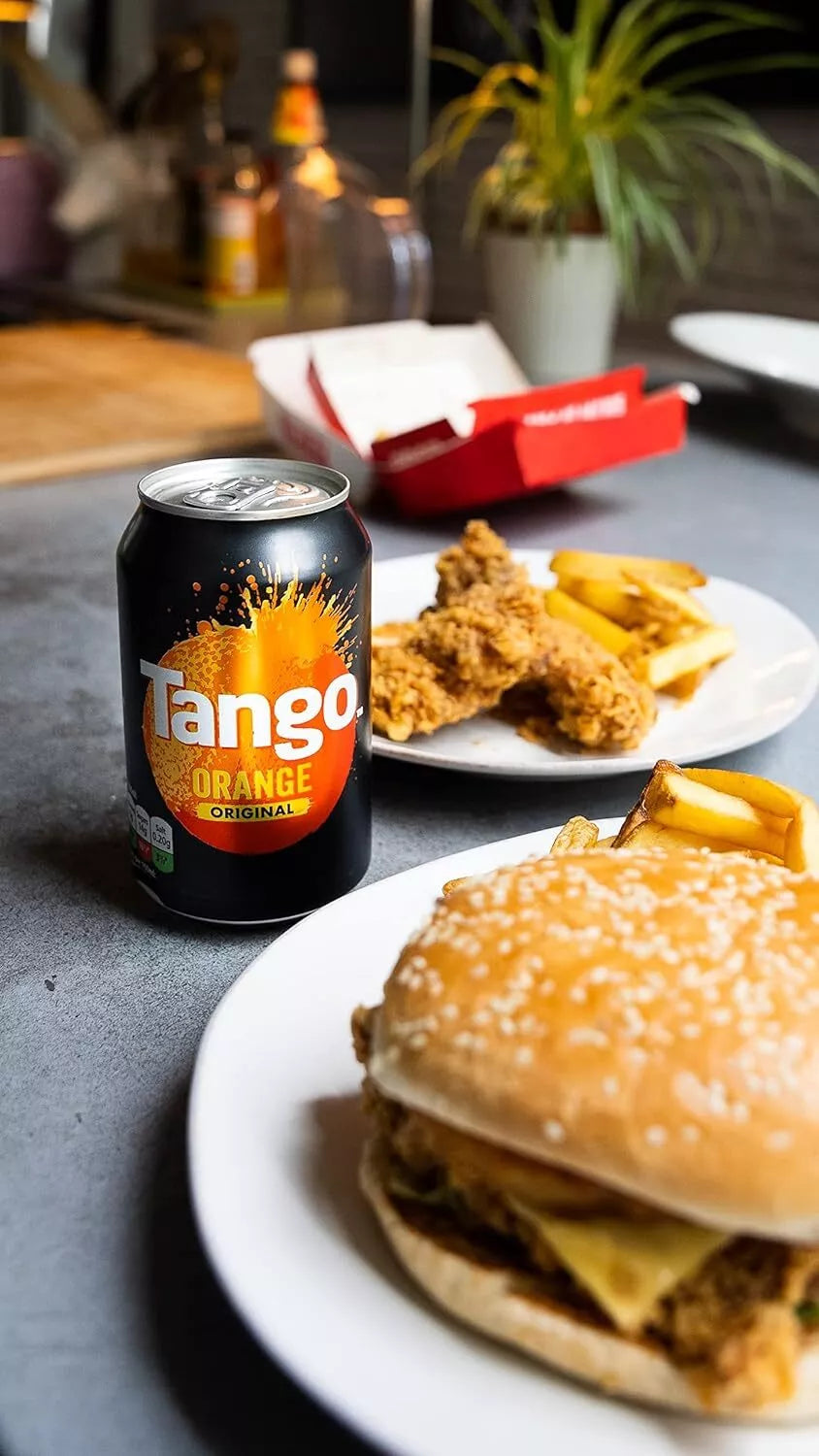 Burger, fries, and Tango Orange can on a table with a plant in the background