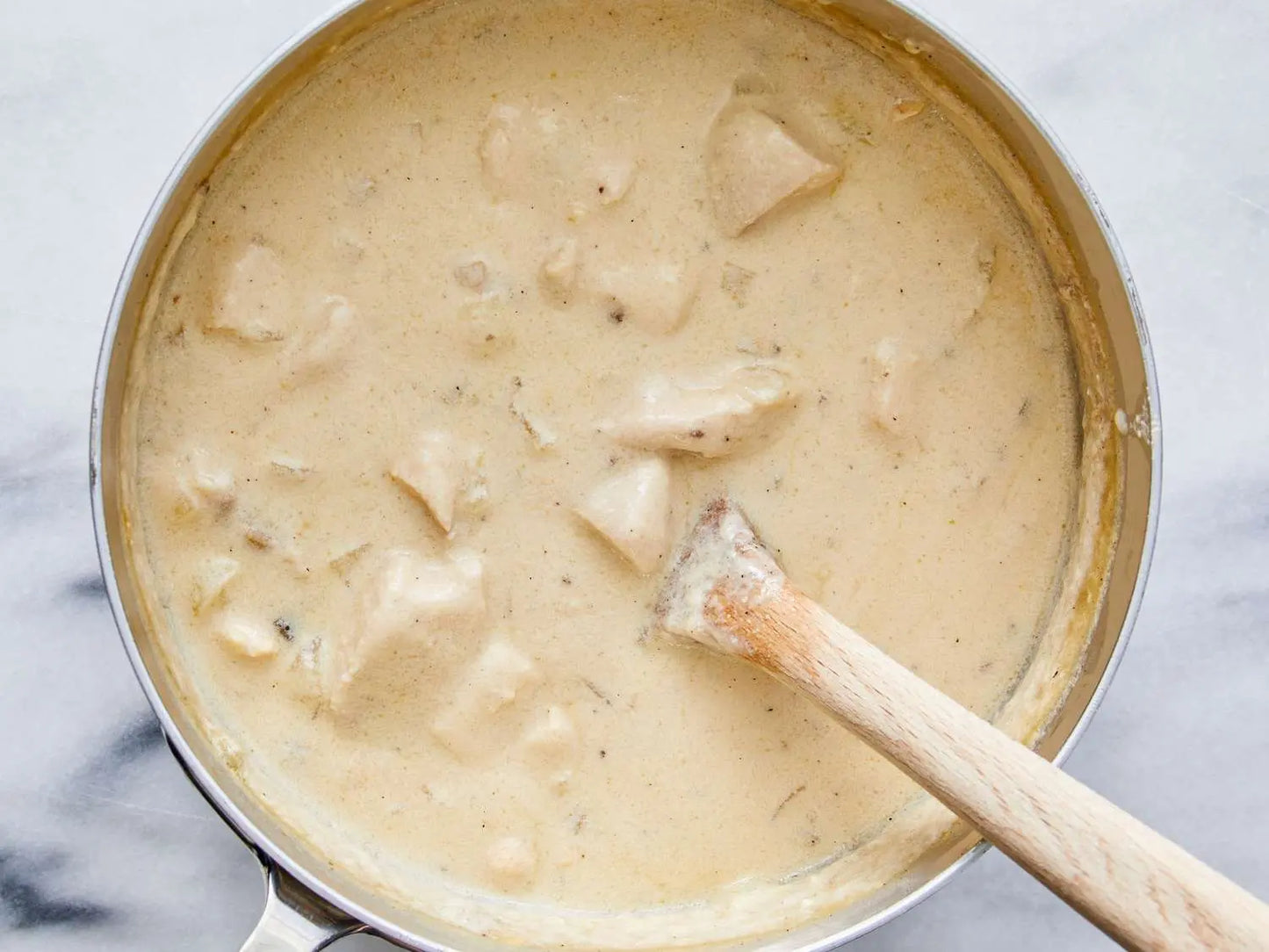 Creamy chicken and dumplings in a saucepan with a wooden spoon.