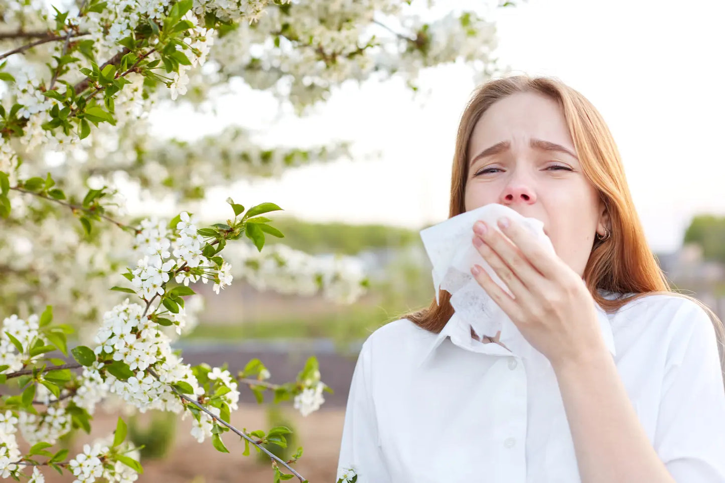 Woman with a runny nose in front of a flowering tree