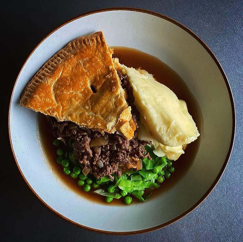 Pie, mashed potatoes, and peas on a plate with a dark background