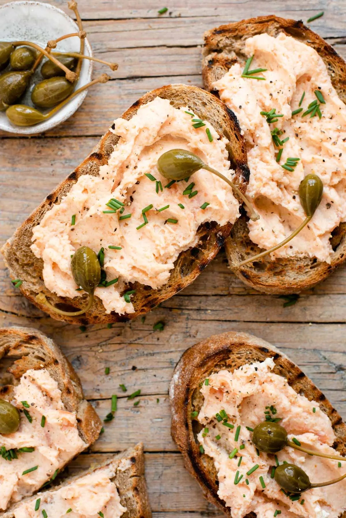 Toasts with salmon spread and capers on a wooden surface