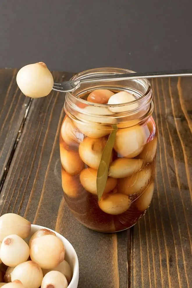 Jar of pickled onions with a spoon on a wooden surface