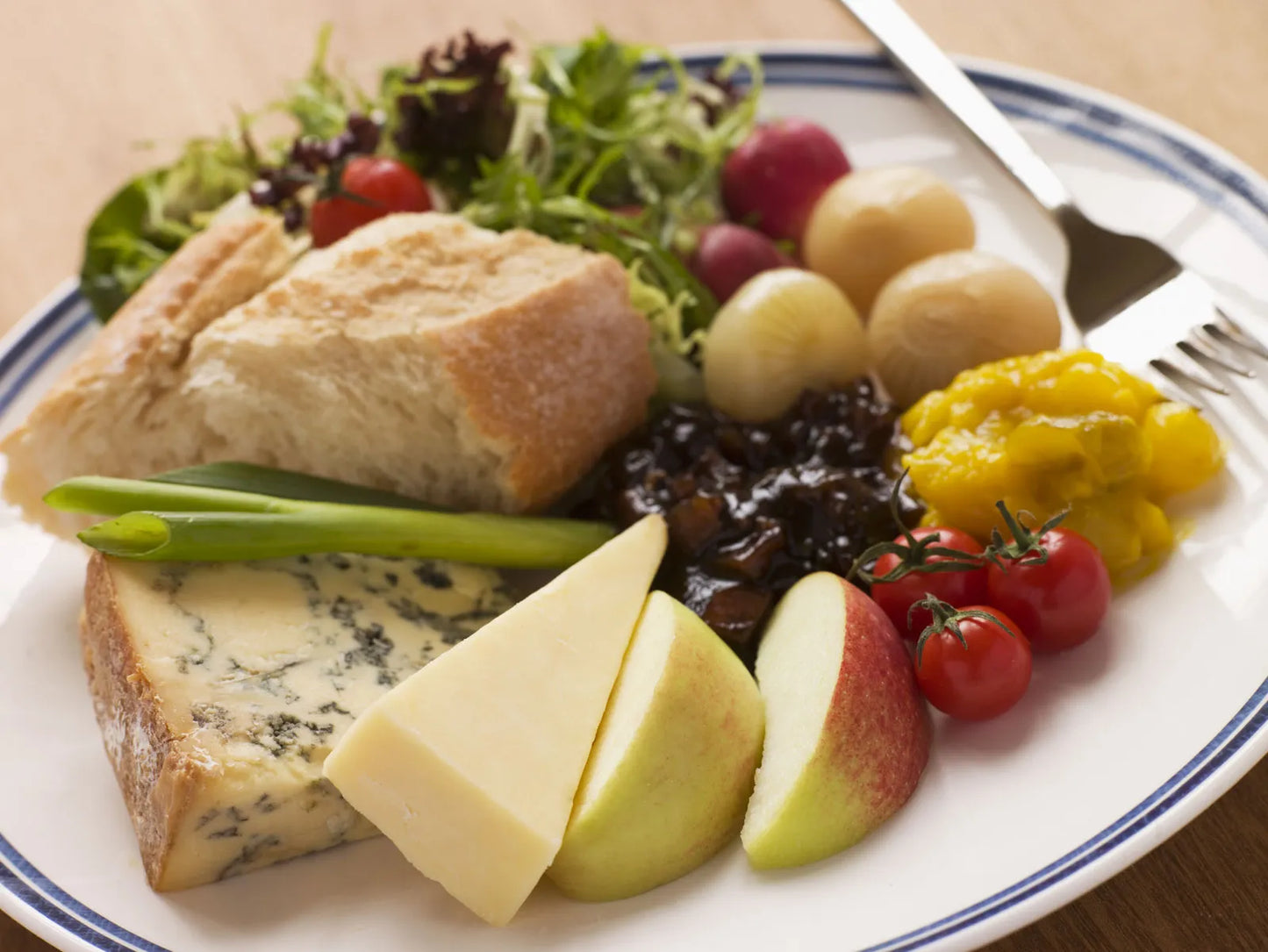Plated meal with bread, cheese, fruits, and vegetables on a white plate with blue rim.