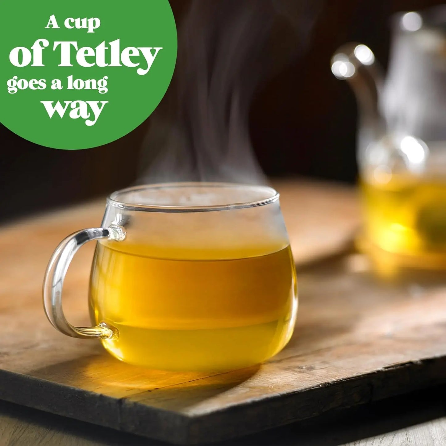 Steaming cup of tea on a wooden surface with a teapot in the background, featuring Tetley branding.