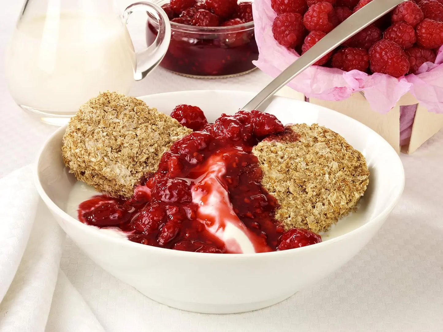 Bowl of dessert with red fruit sauce and crumbly topping on a white surface.