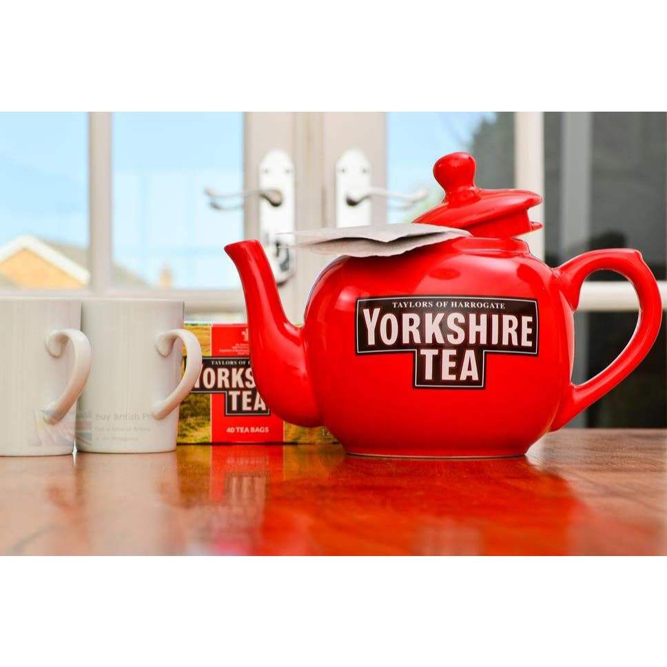 Red Yorkshire Tea teapot on a wooden surface with tea bags in the background.