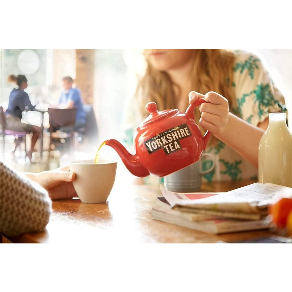 Person pouring tea from a red Yorkshire Tea teapot into a cup.