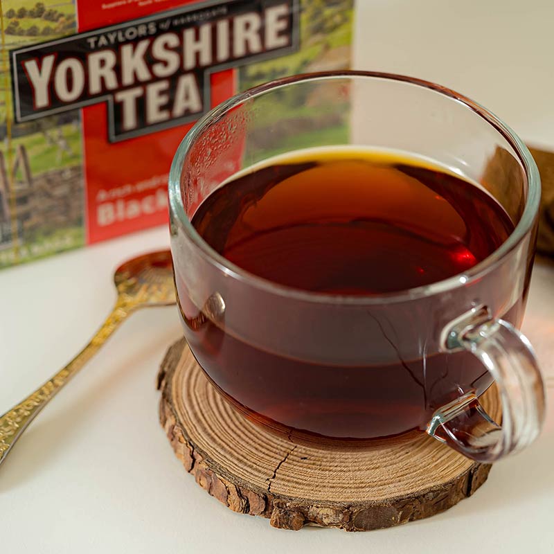 Glass mug of black tea on a wooden coaster with a Yorkshire Tea box in the background.
