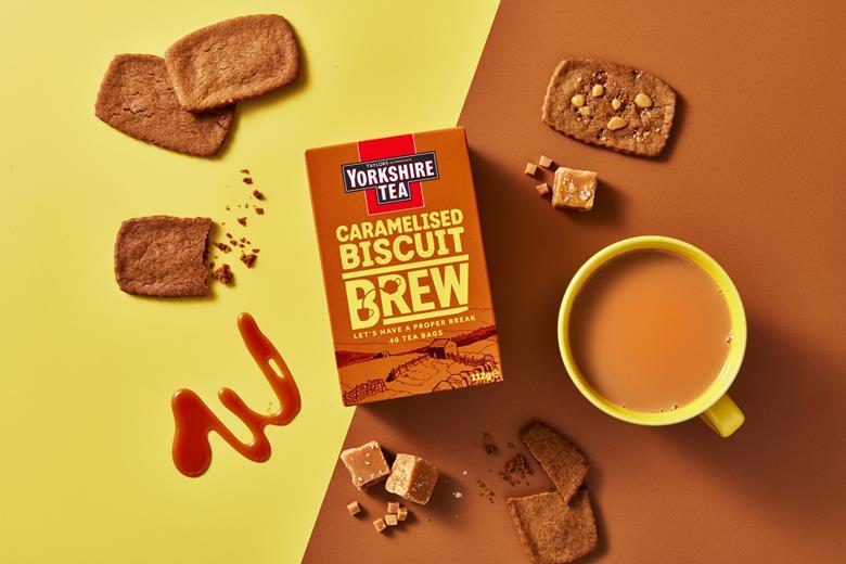 Yorkshire Tea Caramelised Biscuit Brew box with a cup of tea and biscuits on a two-tone background