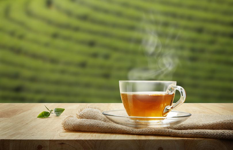 Steaming cup of tea on a wooden table with a blurred green landscape in the background