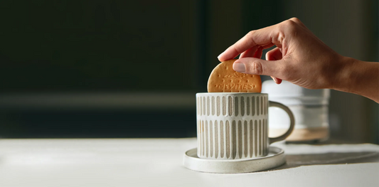 Hand dipping a McVitie’s Digestive biscuit into a mug of tea – a classic British tea-time tradition.