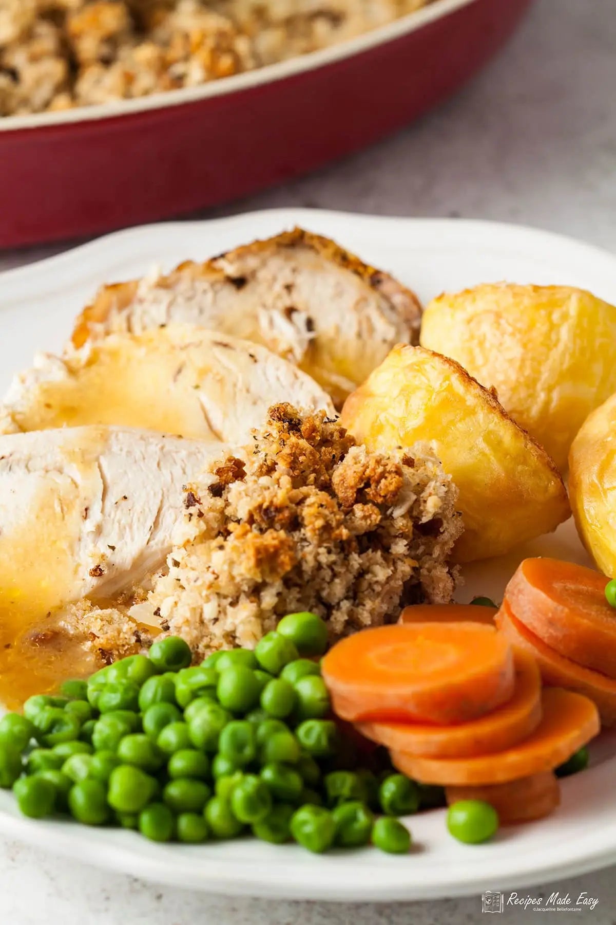 Plated dish with roasted chicken, stuffing, carrots, peas, and Yorkshire pudding.