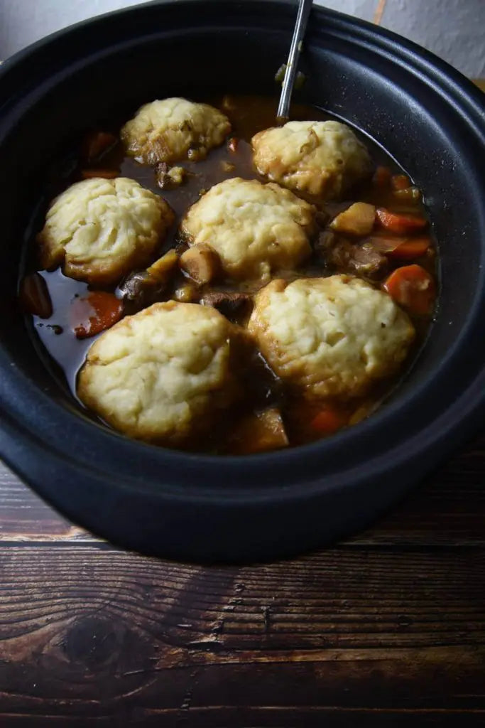 Stew with Aunt Bessie's dumplings in a black bowl on a wooden surface