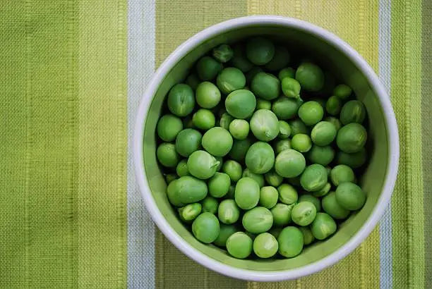 White bowl filled with green peas on a green striped fabric background