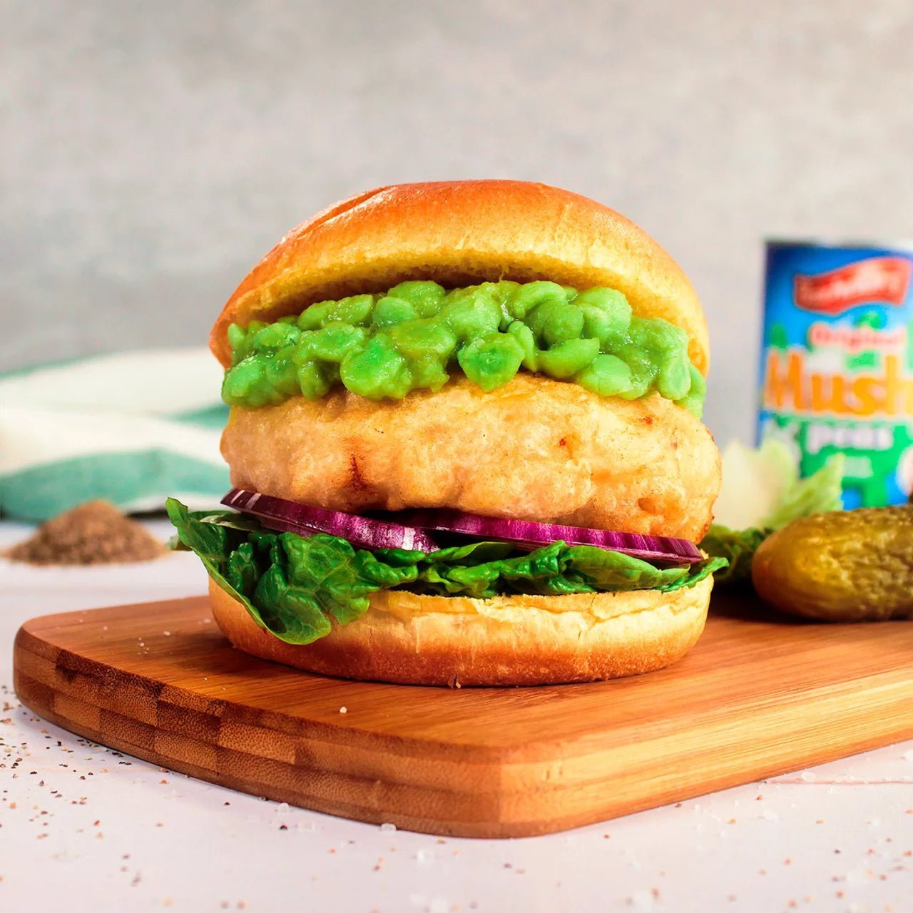 Burger with green patty, lettuce, and onion on a wooden cutting board.