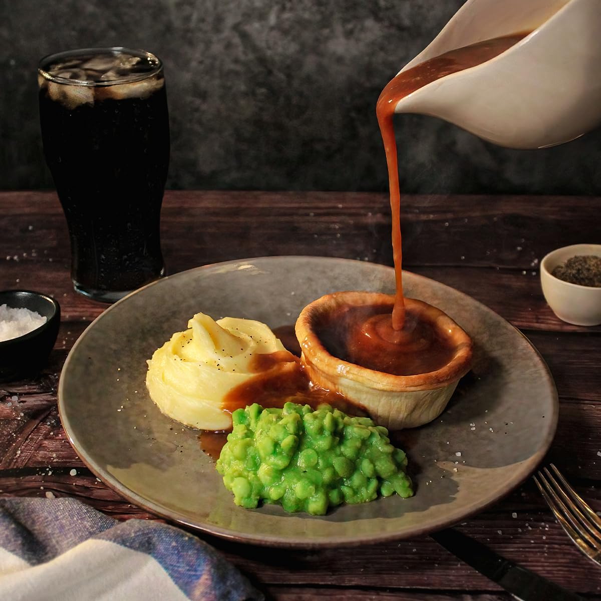 Traditional British meal with pie, mushy peas, and a pint of beer on a wooden table.