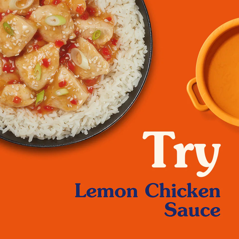 Lemon chicken dish on rice with a bowl of sauce on an orange background