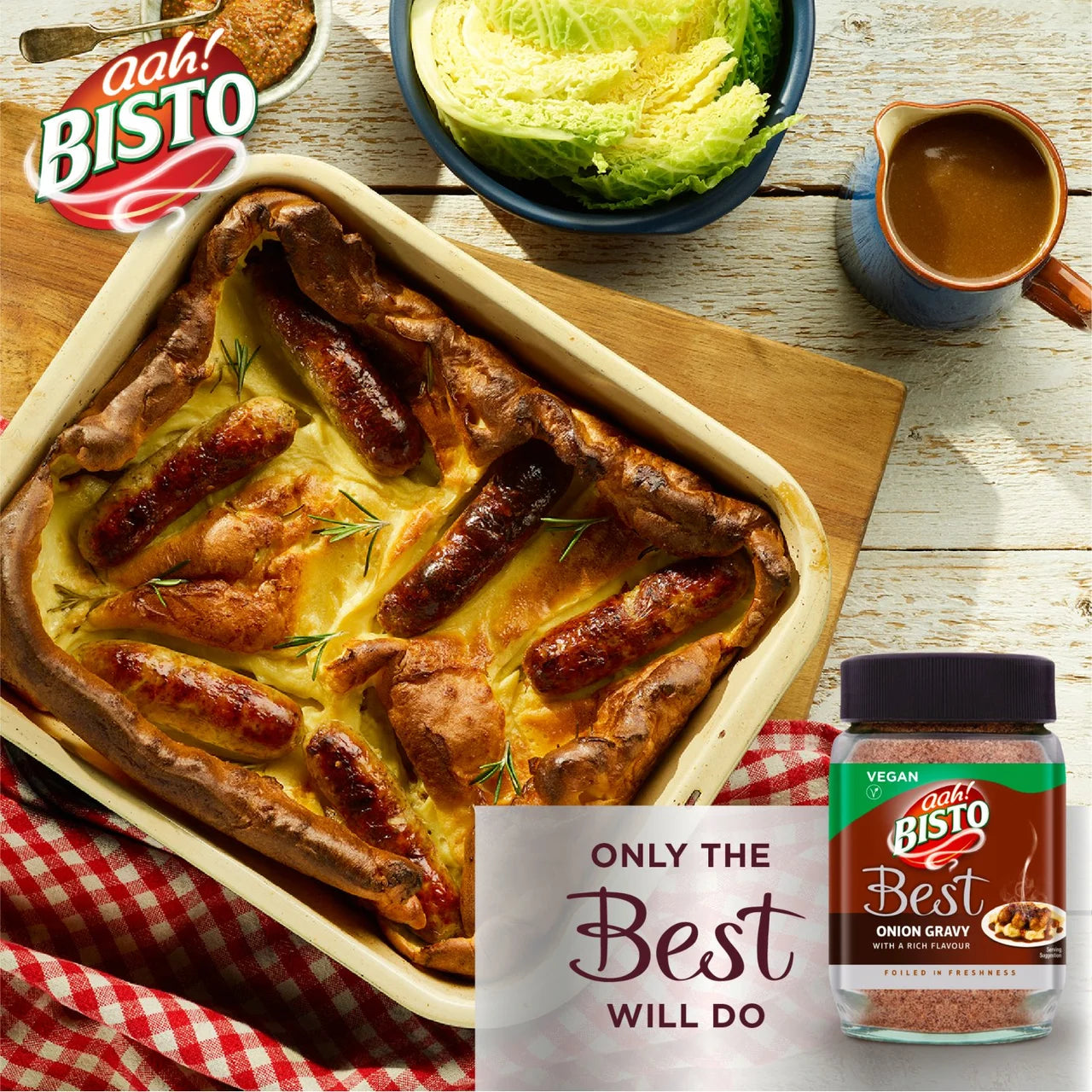 Bisto Best Onion Gravy container with a dish of baked sausages and Yorkshire pudding on a wooden table.